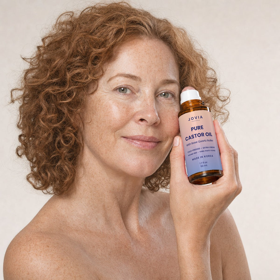 Woman with curly red hair holding Jovia castor oil to her cheek