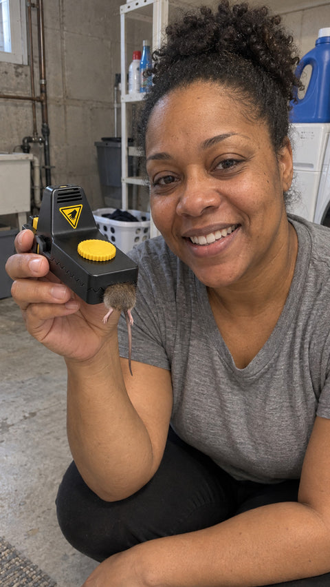Smiling woman in her laundry room holding a Jovia trap with a caught mouse